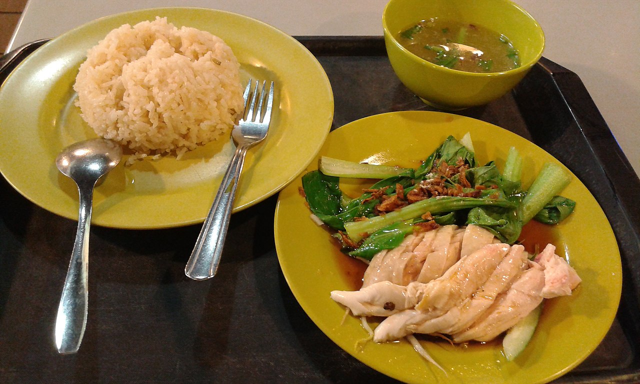 A plate of Hainanese chicken rice with sliced poached chicken, chicken-stock rice and chilli sauce