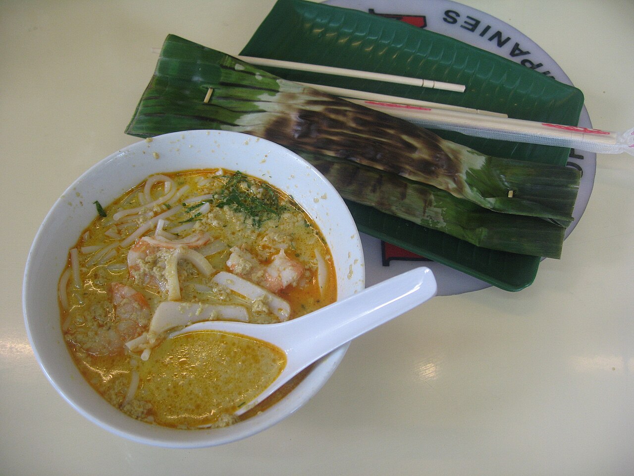 A bowl of Katong laksa in coconut curry broth served with otah-otah on a banana leaf