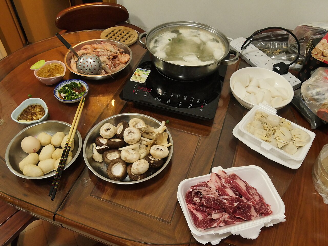 A bubbling Chinese steamboat surrounded by plates of raw meat, vegetables and dipping sauces