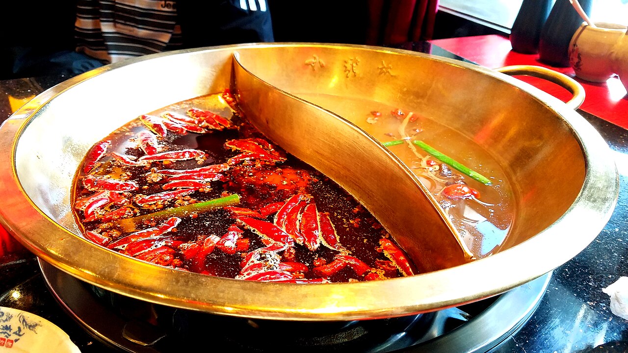 A yuanyang twin hot pot with bright red Sichuan ma la broth on one side and clear broth on the other