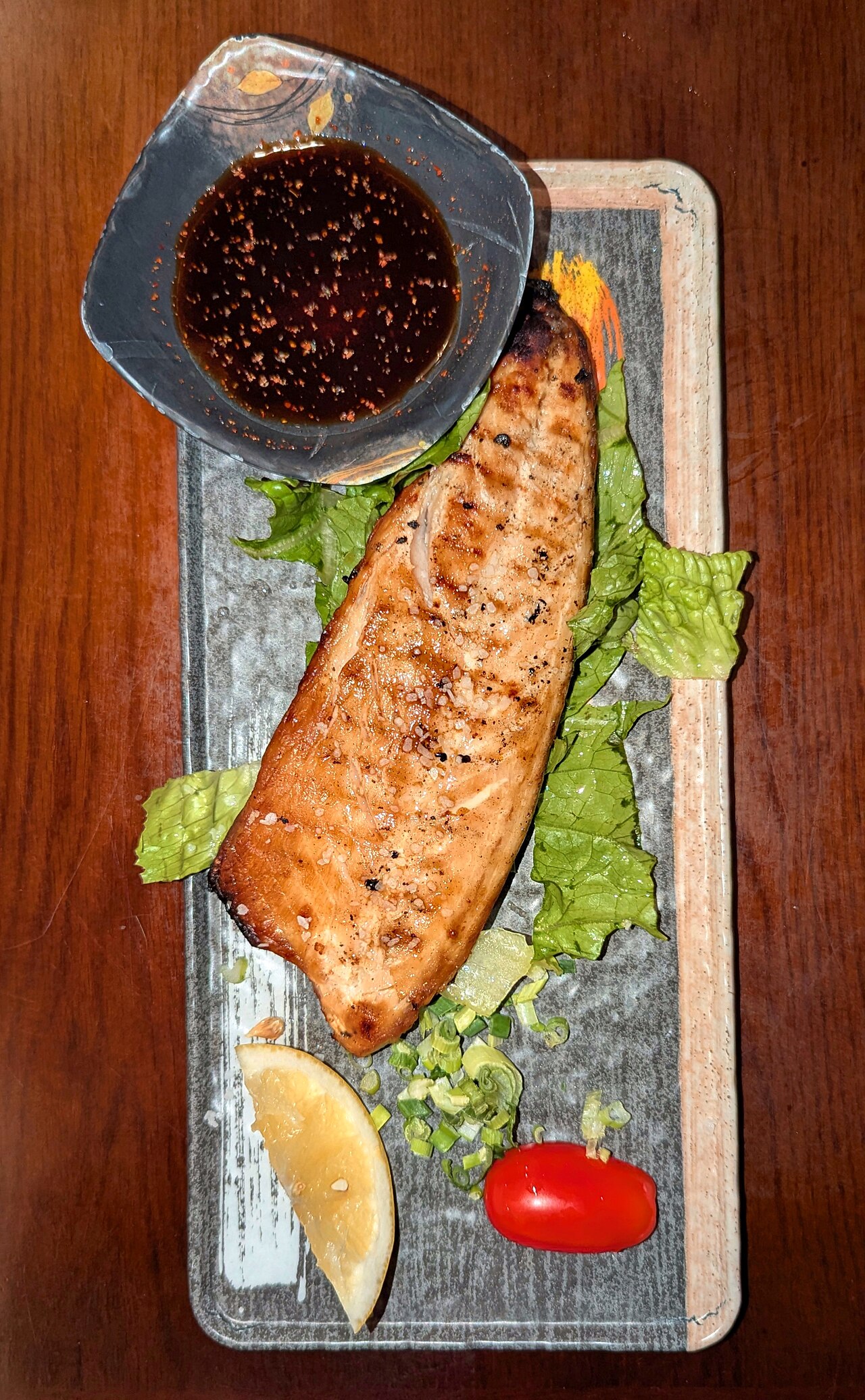 A salt-grilled saba mackerel fillet served on a plate, crispy skin facing up