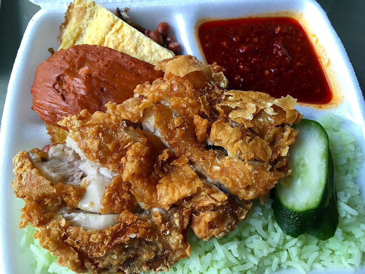 A plate of nasi lemak with chicken cutlet, sambal, peanuts, egg and cucumber