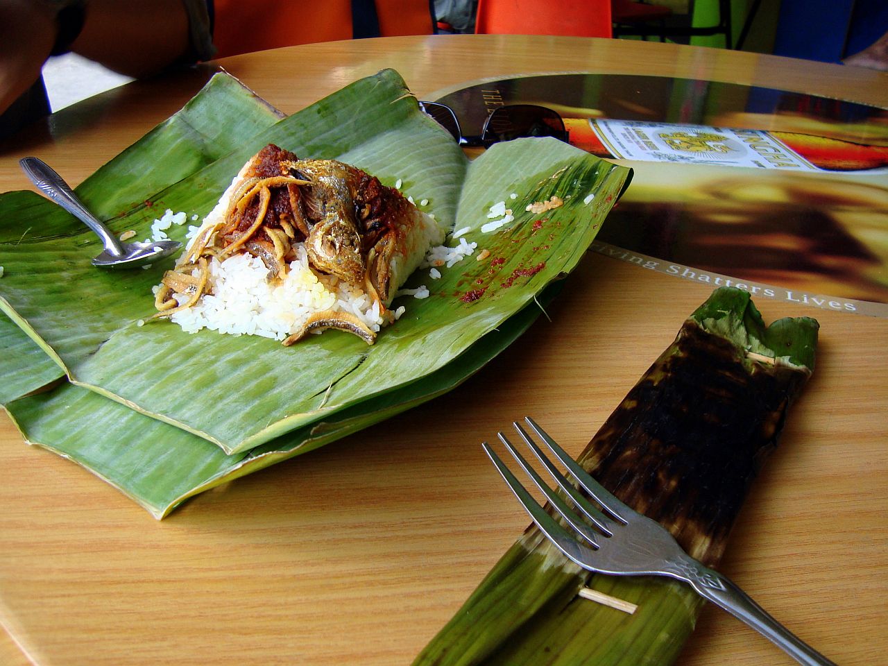 Coconut rice with sambal, fried fish and fried anchovies wrapped in a banana leaf parcel with otah-otah alongside